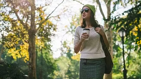 Woman holding coffee walking through park